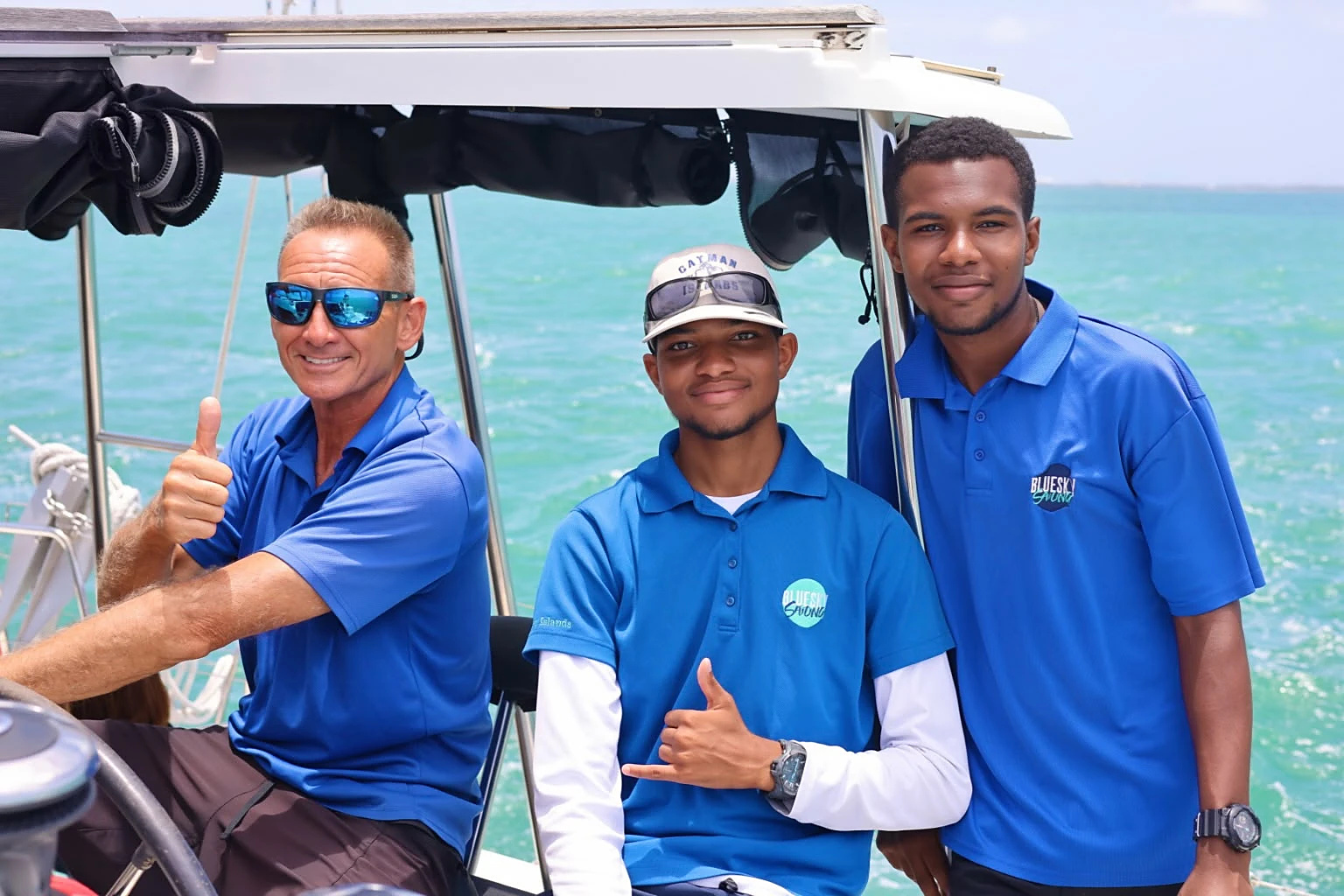 Three Blue Sky Sailing crew members in branded polo shirts at the helm of the catamaran