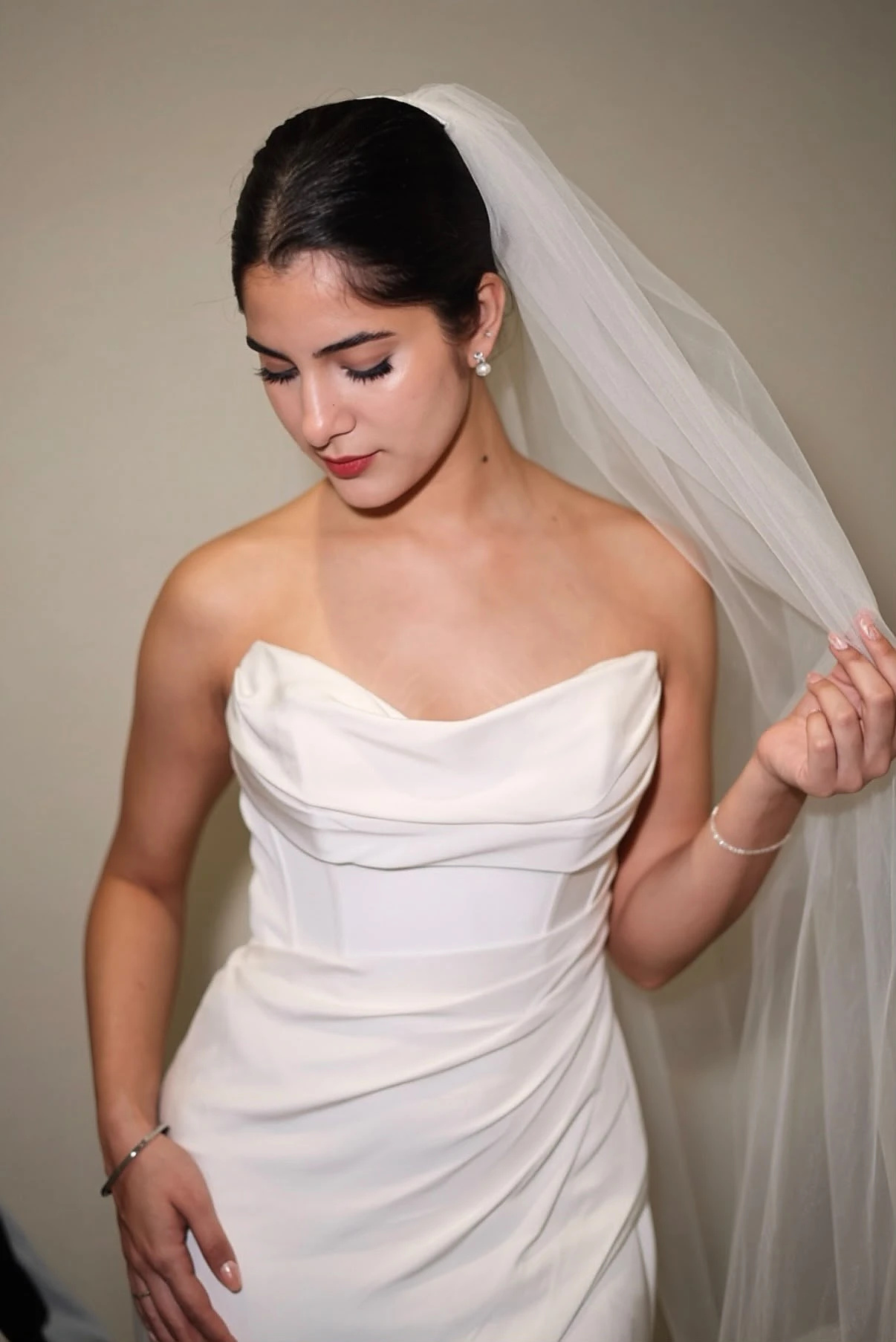A model in a strapless draped ivory gown holding a long tulle veil